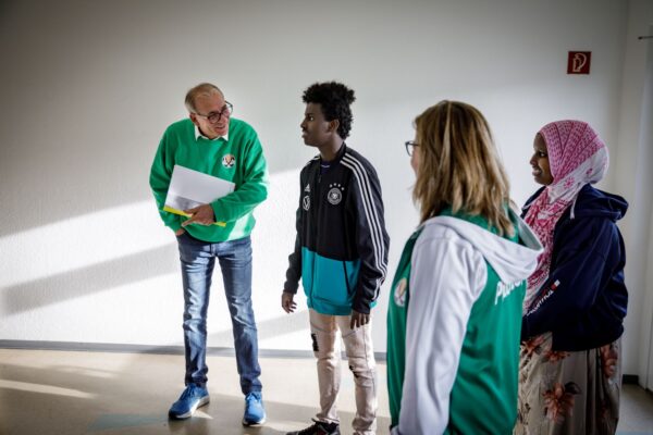 zwei Ehrenamtliche unterhalten sich mit zwei jungen Geflüchteten in einem Raum